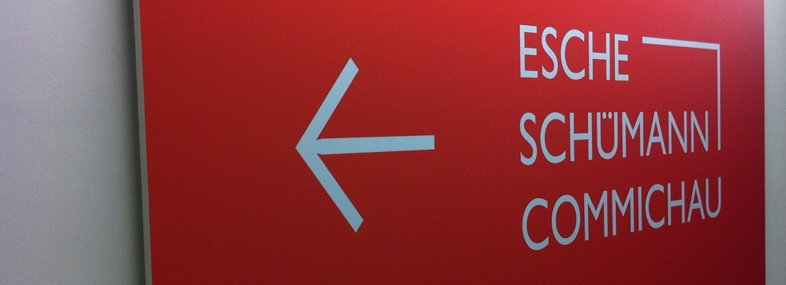 Rotes Wandschild mit weißem Pfeil und Beschriftung Esche Schümann Commichau – Folien Fischer Hamburg